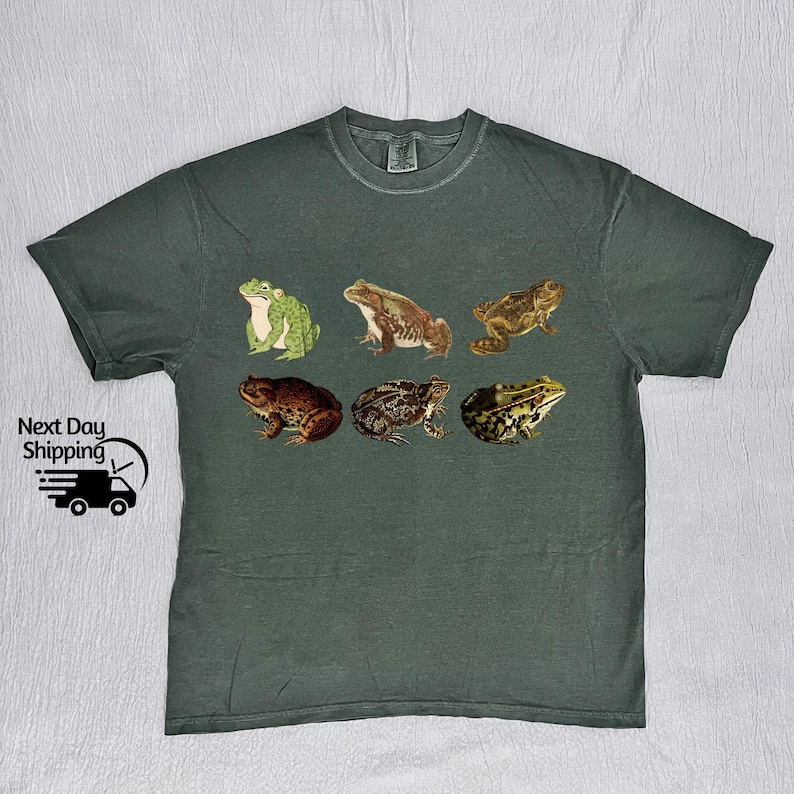 May include: A dark green t-shirt with a vintage illustration of six frogs in different poses. The frogs are in shades of green, brown, and tan.