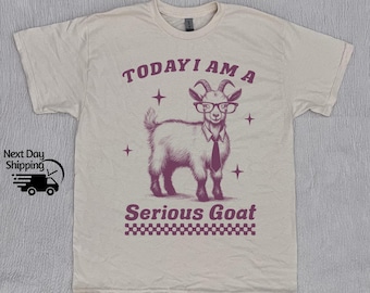 May include: A beige t-shirt with a pink goat wearing glasses and a tie. The text "TODAY I AM A SERIOUS GOAT" is printed on the shirt.