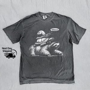 May include: A dark gray t-shirt with a graphic of a sloth riding a turtle, which is riding another turtle. The text "WHEEEEE!" is above the sloth.