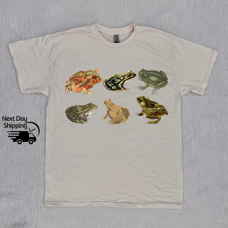 Puede incluir: Una camiseta beige claro con un estampado gr&aacute;fico de seis ranas diferentes en varios colores y poses. Las ranas est&aacute;n todas mirando hacia adelante y tienen diferentes expresiones.