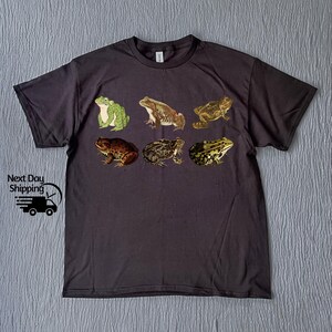 May include: A dark gray t-shirt with a print of six different frogs in various poses. The frogs are green, brown, and black.