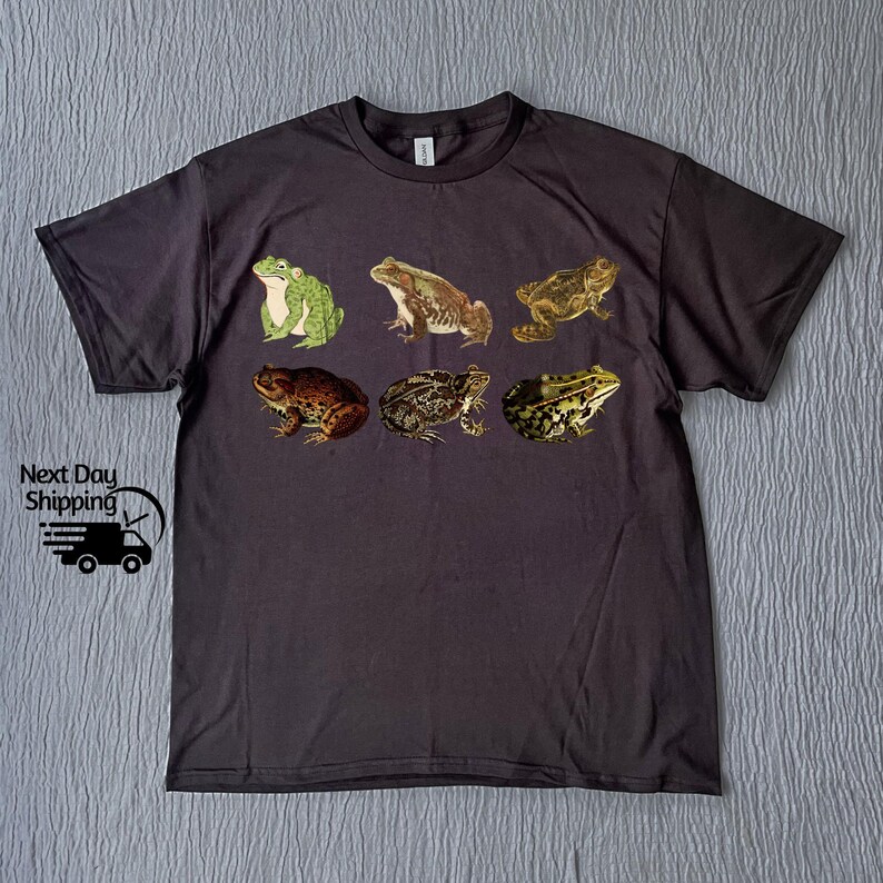 May include: A dark gray t-shirt with a print of six different frogs in various poses. The frogs are green, brown, and black.