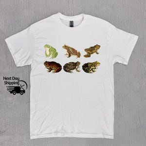 May include: White t-shirt with a graphic of six different frogs in various poses. The frogs are brown, green, and tan.