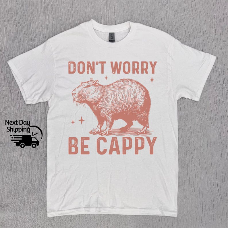 May include: White t-shirt with a pink graphic of a capybara and the text "Don't Worry Be Cappy".