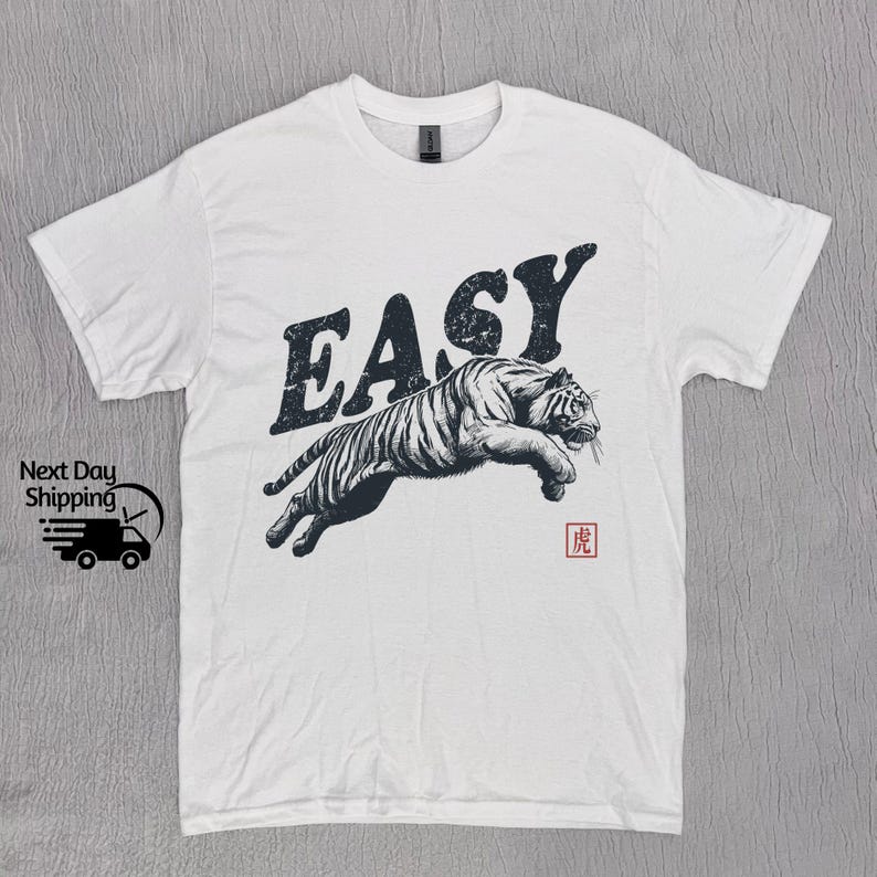 K&ouml;nnte beinhalten: Wei&szlig;es T-Shirt mit einem schwarz-wei&szlig;en Tiger-Motiv und dem Wort "EASY" in gro&szlig;en, fetten Buchstaben. Der Tiger springt und das Wort "EASY" befindet sich dar&uuml;ber. In der rechten unteren Ecke befindet sich ein kleines rotes Quadrat mit einem japanischen Schriftzeichen.
