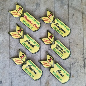 May include: Six yellow and green fabric patches with the text "PROPERTY OF 103!" and names like "Pearlie Cat", "Jack", "Smyton", "Director of Education", "Jason", and "Jess". Each patch has a small red and yellow "sweet dreams" patch attached.