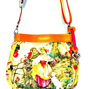 以下が含まれることがあります： カラフルな牧歌的なシーンのプリントが施された黄色のクロスボディバッグ。バッグは、赤とオレンジのストラップ、ハート型のチャーム、オレンジ色のレザートリムが特徴です。プリントは、犬と一緒に庭にいる人物を描いています。