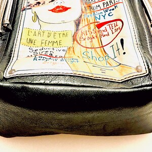 Pode incluir: Bolsa de m&atilde;o de couro preta com uma ilustra&ccedil;&atilde;o colorida. A ilustra&ccedil;&atilde;o apresenta o rosto de uma mulher com l&aacute;bios vermelhos e o texto "MAKEUP TIPS FROM PARIS" e "KISS and TELL Bright Red Lips". A bolsa tem fecho de z&iacute;per.