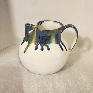 May include: White ceramic pitcher with a blue and green glaze. The glaze has a drip effect, creating a unique and artistic look.