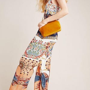May include: A woman wearing a white and blue patterned jumpsuit with a yellow velvet clutch bag.