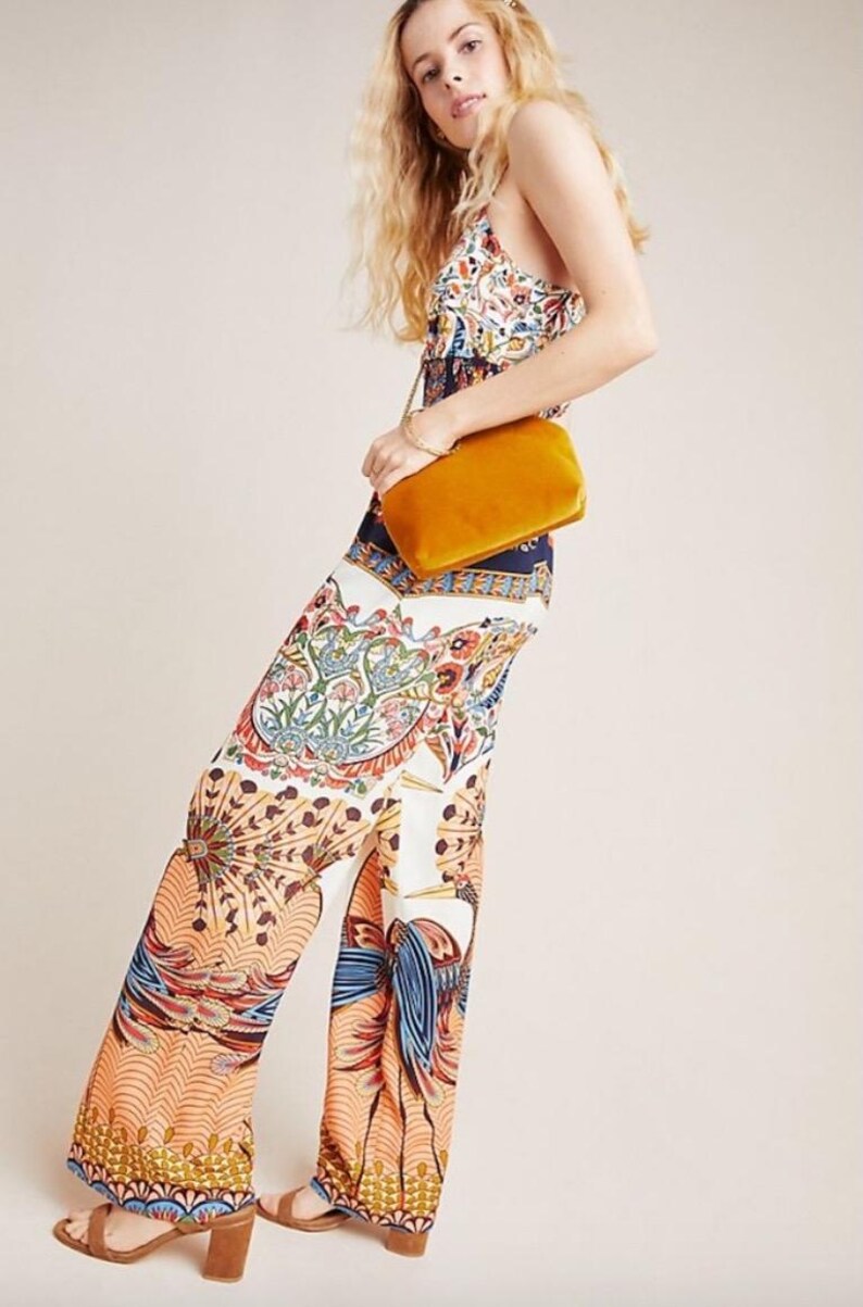 May include: A woman wearing a white and blue patterned jumpsuit with a yellow velvet clutch bag.