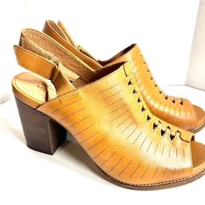May include: A pair of open-toe, tan leather slingback heels. The shoes feature a peep-toe design with cut-out detailing, a thick wooden heel, and an adjustable ankle strap. The heels measure approximately 3 inches.