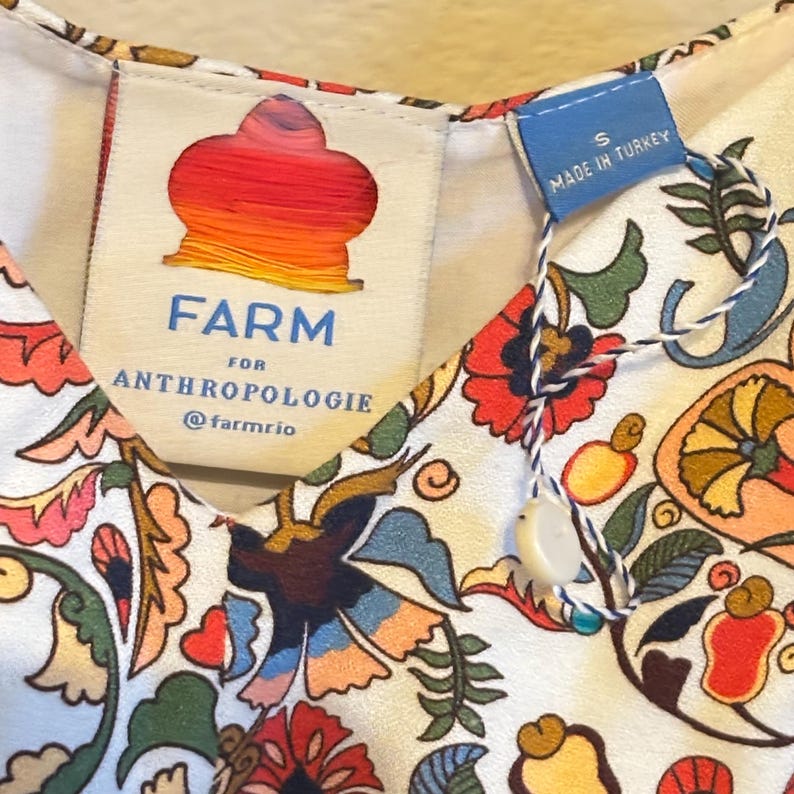 May include: A white dress with a colorful floral print. The dress has a V-neck and is made by FARM for Anthropologie. The tag says "Made in Turkey" and "S".