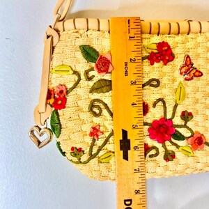 Puede incluir: Un bolso de paja con un dije de coraz&oacute;n y bordado floral. El bolso mide 17,8 cm de largo y presenta flores rosas, rojas y verdes.