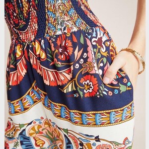May include: A blue and white patterned jumpsuit with a floral design. The jumpsuit has a fitted bodice and wide legs. The fabric is lightweight and flowy.