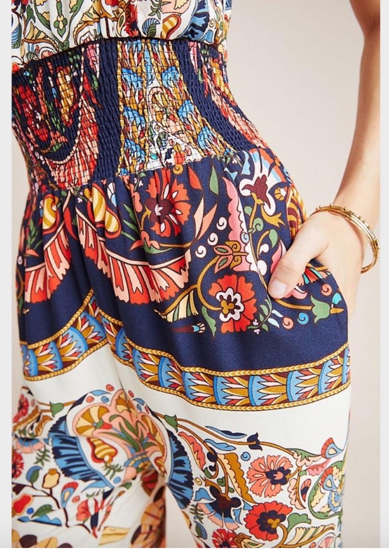 May include: A blue and white patterned jumpsuit with a floral design. The jumpsuit has a fitted bodice and wide legs. The fabric is lightweight and flowy.