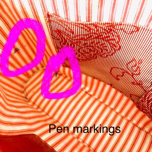 May include: Close-up of a red and white striped fabric, likely the lining of a bag. The fabric features a traditional stripe design in red and white. The text "Pen markings" is present.