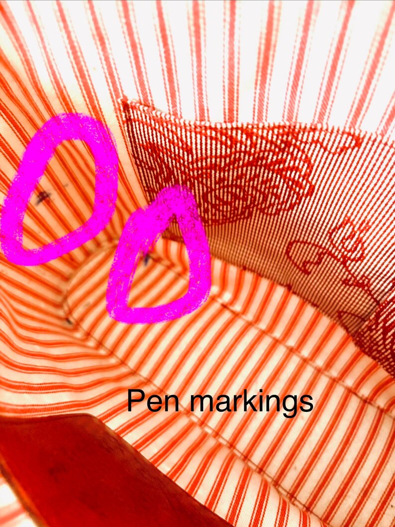 May include: Close-up of a red and white striped fabric, likely the lining of a bag. The fabric features a traditional stripe design in red and white. The text "Pen markings" is present.
