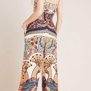 May include: A white jumpsuit with a colorful floral and bird print. The jumpsuit has a fitted bodice and wide-leg pants.