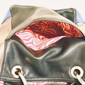 Pode incluir: Bolsa de couro preta com ferragens prateadas, fecho de correr e forro com estampa de zebra vermelha e branca. A bolsa apresenta uma combina&ccedil;&atilde;o de pain&eacute;is de couro preto, bege e azul. A bolsa tem uma al&ccedil;a de ombro.