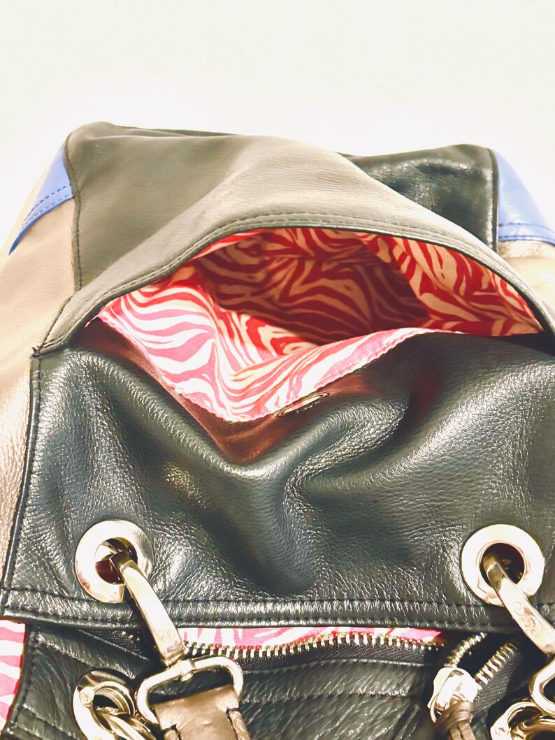 Pode incluir: Bolsa de couro preta com ferragens prateadas, fecho de correr e forro com estampa de zebra vermelha e branca. A bolsa apresenta uma combina&ccedil;&atilde;o de pain&eacute;is de couro preto, bege e azul. A bolsa tem uma al&ccedil;a de ombro.