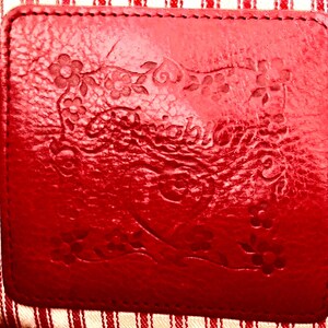 May include: A close-up of a red leather label with embossed floral designs and text. The label is stitched onto a red and white striped fabric. The textures and patterns create a vintage aesthetic. The overall look is handcrafted.