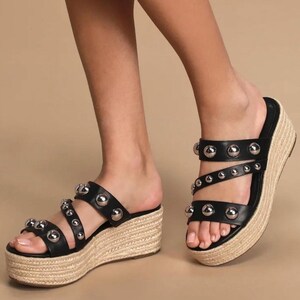May include: Black leather wedge sandals with silver studded straps. The sandals have a thick platform sole and a jute-wrapped wedge heel.