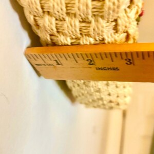 Puede incluir: Primer plano de un objeto rectangular tejido de color crema medido con una regla de madera marcada en pulgadas. La regla muestra que el objeto tiene aproximadamente 2 pulgadas de ancho.