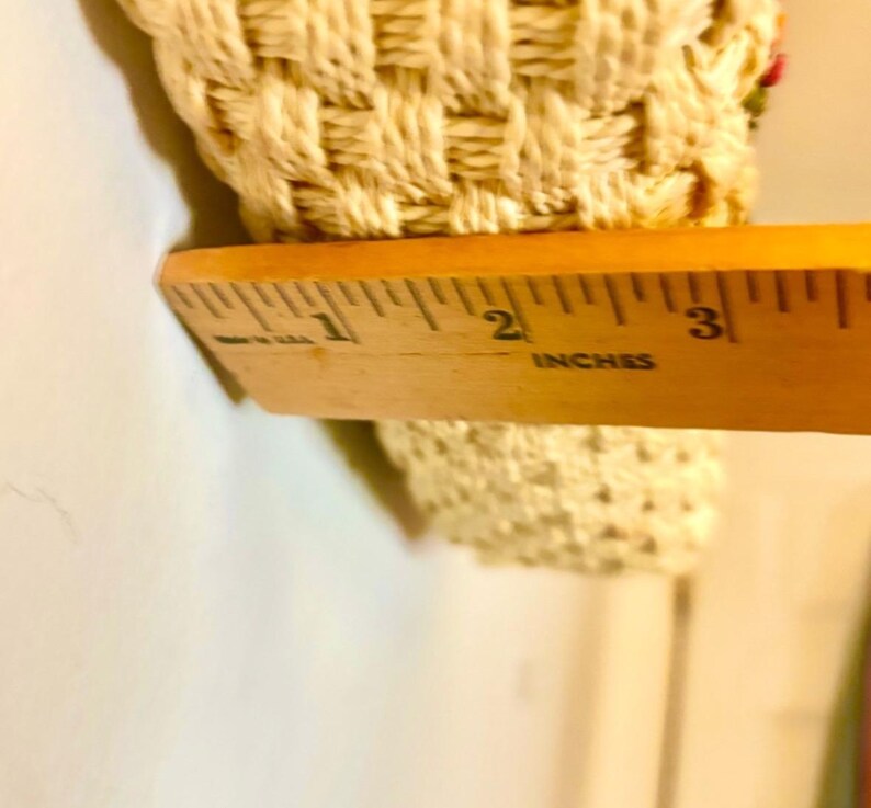 Puede incluir: Primer plano de un objeto rectangular tejido de color crema medido con una regla de madera marcada en pulgadas. La regla muestra que el objeto tiene aproximadamente 2 pulgadas de ancho.