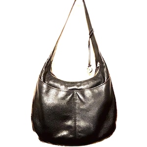 May include: Black leather hobo bag with a single shoulder strap. The bag has a curved shape with a front pocket and a zipper closure. A small charm hangs from the strap. The leather has a textured appearance.