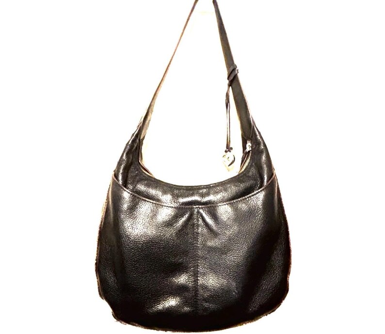 May include: Black leather hobo bag with a single shoulder strap. The bag has a curved shape with a front pocket and a zipper closure. A small charm hangs from the strap. The leather has a textured appearance.