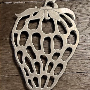 May include: Silver-toned metal strawberry-shaped hot pad with a cutout design.