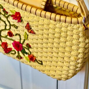 Puede incluir: Un bolso de paja tejido con un asa de cuero marr&oacute;n claro y un dise&ntilde;o floral. Las flores son rojas, rosas y verdes.
