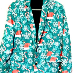 May include: A teal Christmas-themed blazer with a festive pattern. The jacket features red Santa hats, candy canes, snowflakes, and gold stars. The blazer is buttoned and hanging on a black hanger.
