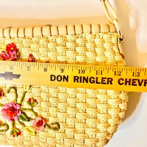 Puede incluir: Un bolso de paja tejido con una correa de cuero marr&oacute;n claro y bordado floral. El bolso mide aproximadamente 28 cm de ancho.