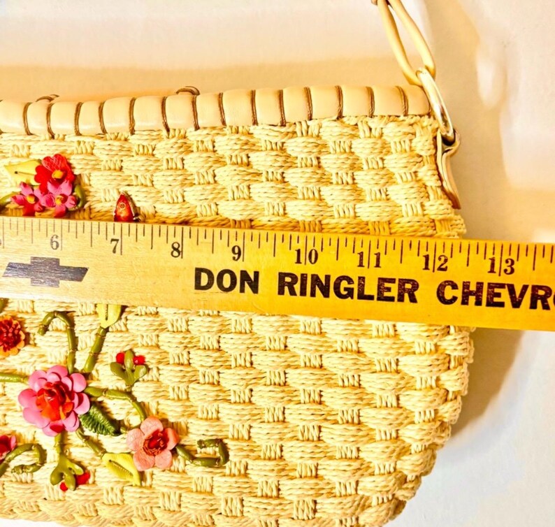 Puede incluir: Un bolso de paja tejido con una correa de cuero marr&oacute;n claro y bordado floral. El bolso mide aproximadamente 28 cm de ancho.