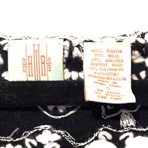 May include: Close-up of a black and white knit garment with a floral design. Two tags are visible, one with the letters "SHRS" in red, and the other with the fabric content: 40% rayon, 35% wool, 20% angora rabbit hair, and 5% cashmere.