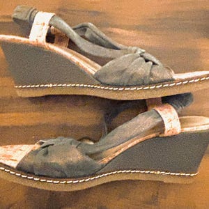 May include: A pair of wedge sandals with a dark gray fabric upper and a cork-like footbed. The sandals have a slingback strap and a stitched sole. The wedge heel is approximately 3 inches high.
