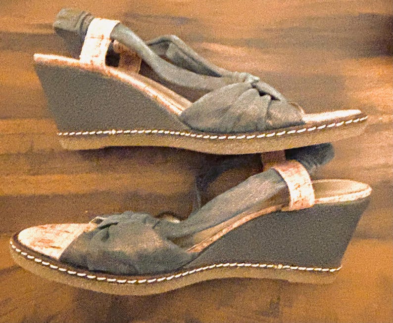 May include: A pair of wedge sandals with a dark gray fabric upper and a cork-like footbed. The sandals have a slingback strap and a stitched sole. The wedge heel is approximately 3 inches high.