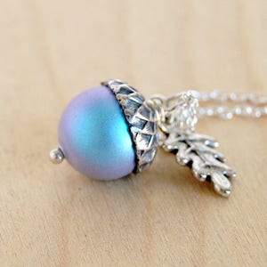 Op de afbeelding: Een zilveren ketting met een blauwe, iriserende eikelbedel en een zilveren eikenbladbedel.