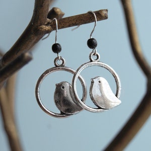 May include: Silver tone earrings with a circle design featuring two birds. The birds are facing each other and are in a circle.