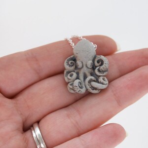 Op de afbeelding: Een zilveren ketting met een grijze keramische octopus hanger. De octopus heeft gedetailleerde tentakels en een getextureerd oppervlak.