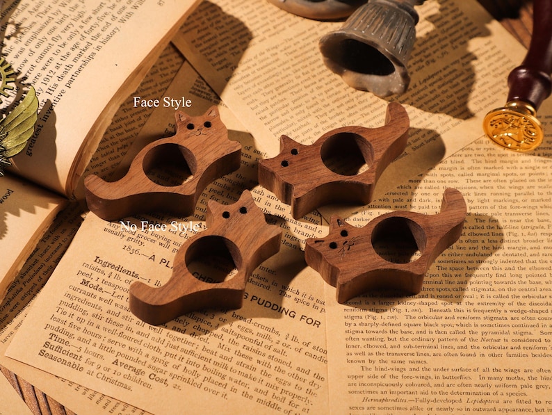 May include: Four wooden cat napkin rings. The rings are carved in the shape of a cat with a hole in the middle for a napkin. The rings are a dark brown colour and have a smooth finish.