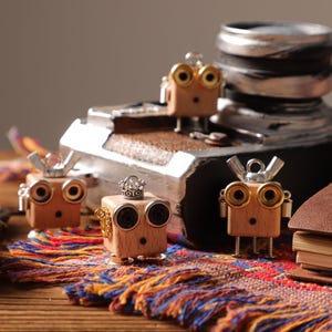 Può includere: Figurine di robot in legno con dettagli in ottone e argento. I robot hanno occhi circolari e sono decorati con corone e altri abbellimenti. Un tessuto colorato e un libro rilegato in pelle sono presenti.