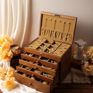 Könnte beinhalten: Eine Holzschmuckschatulle mit mehreren Schubladen und Fächern. Die Schatulle ist geöffnet und zeigt verschiedene Halsketten, Ringe und Armbänder. Der Innenraum ist mit einem beigefarbenen Stoff ausgekleidet, und die Außenseite hat eine warme braune Farbe.