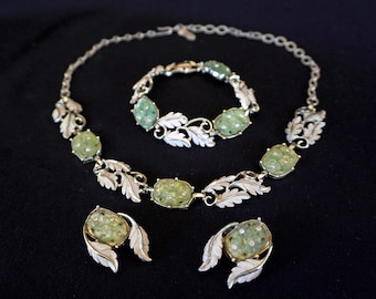 May include: A vintage green and silver necklace, bracelet, and earrings set with a leaf design. The jewelry features green stones set in silver.