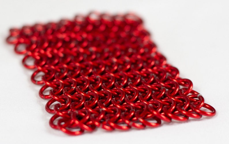 Puede incluir: Un primer plano de una malla de cota de malla roja. La cota de malla est&aacute; hecha de peque&ntilde;os anillos de metal interconectados.