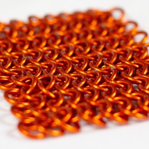 Puede incluir: Primer plano de una pieza de cota de malla naranja, un tipo de armadura de metal tejido.