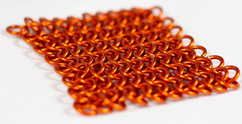 Puede incluir: Primer plano de una pieza de cota de malla naranja, un tipo de armadura de metal tejido.