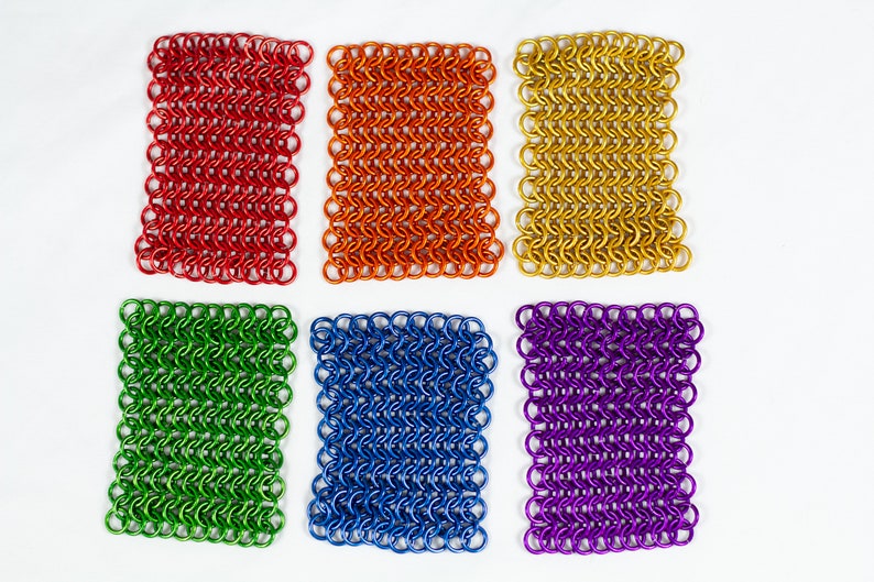 Puede incluir: Seis piezas cuadradas de cota de malla en diferentes colores: rojo, naranja, dorado, verde, azul y morado.